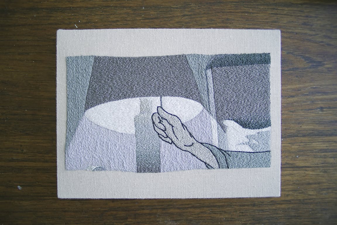 An embroidery shows a hand turning on a lamp.